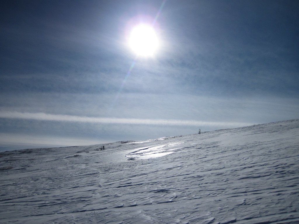 sun shining with glare across snow at the top of Snowmass near ski trail named after John Denver song